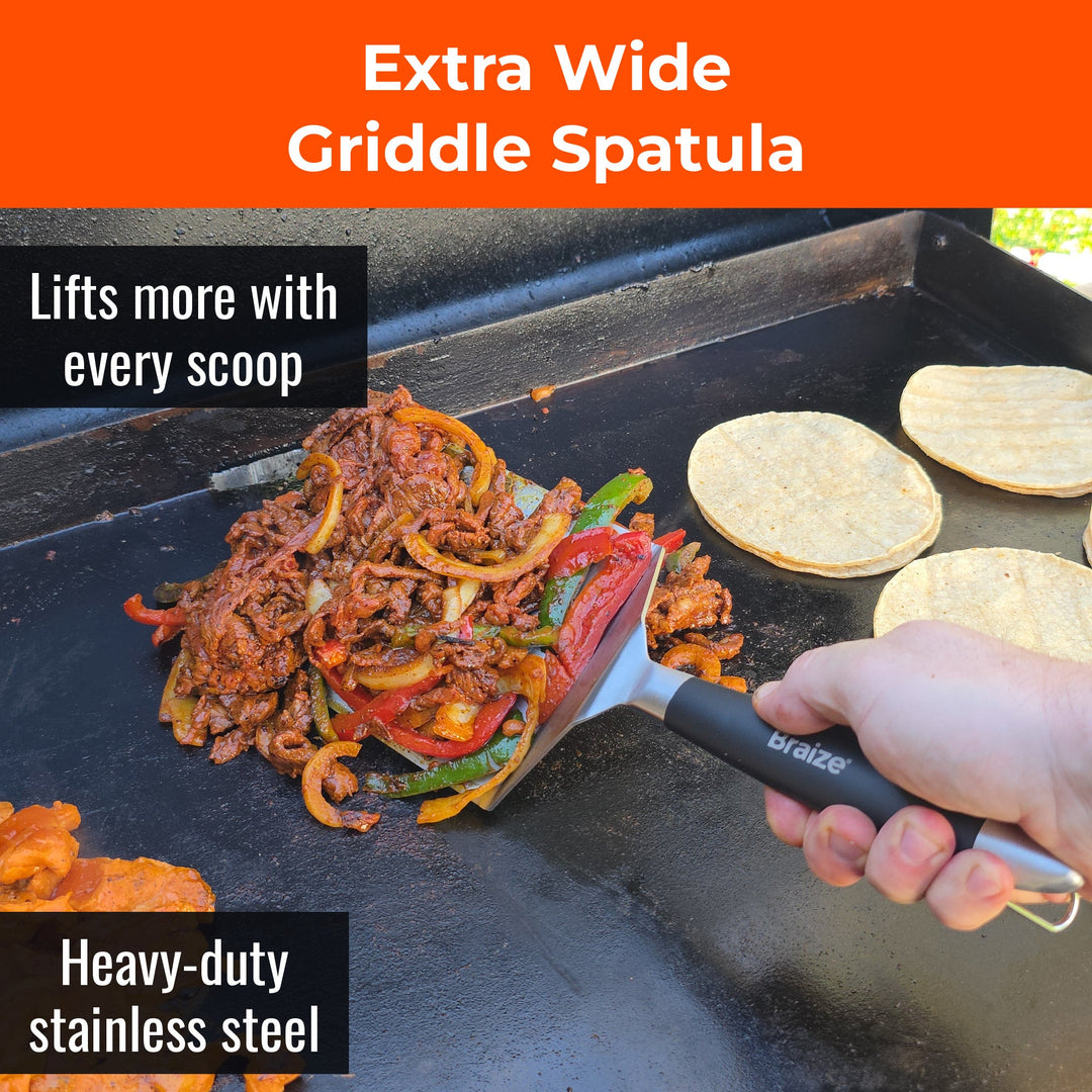 Extra wide spatula lifting a pile of fajita meat and peppers off a flat top griddle