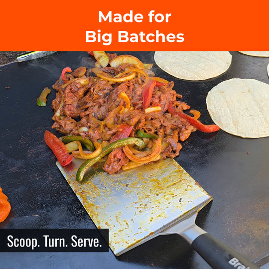 Wide spatula moving a large batch of fajita meat on a griddle